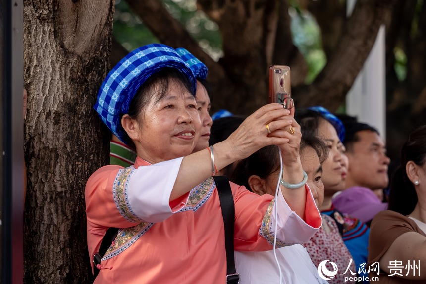 路邊圍觀的少數(shù)民族同胞用手機(jī)記錄巡游盛況。人民網(wǎng)記者 涂敏攝